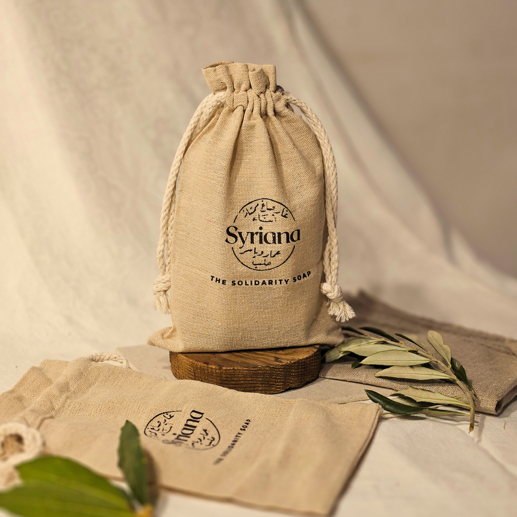 Syriana linen and cotton gift bag standing upright with drawstrings closed next to a flat bag