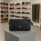 Black leather shoulder bag displayed on a grey pedestal in a boutique setting