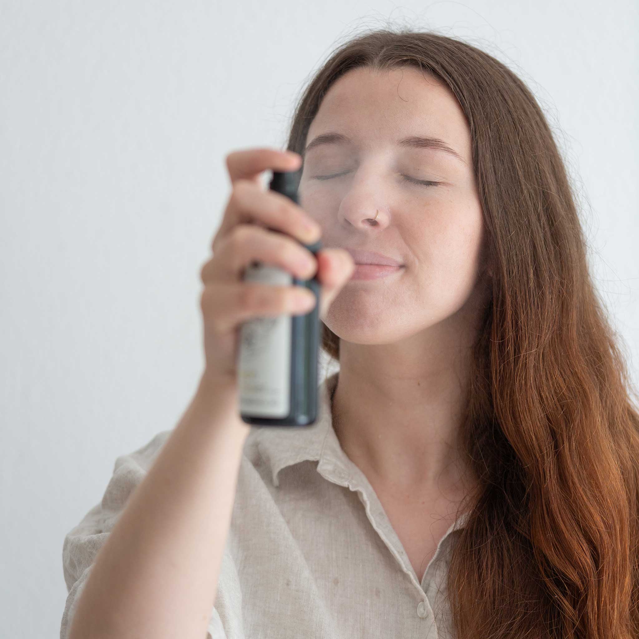 Woman with closed eyes gently spraying rosewater mist onto her face